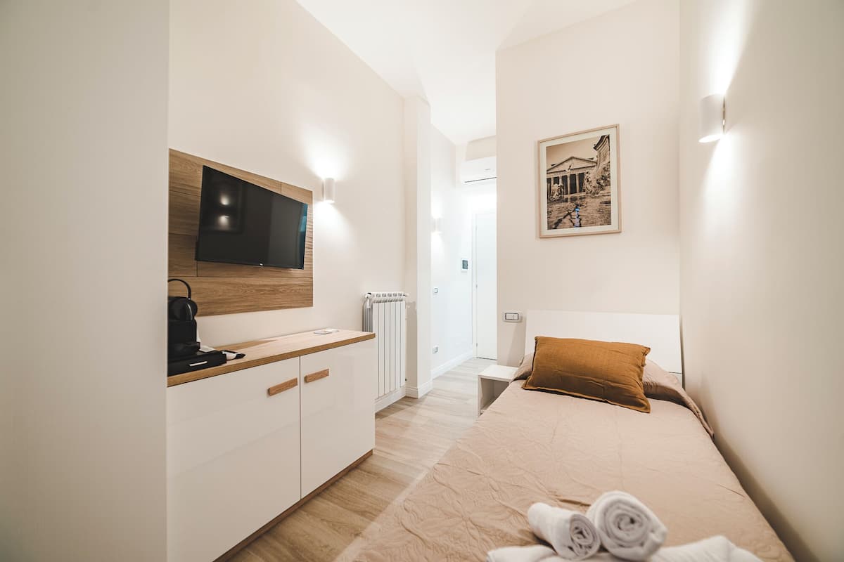 Una habitación de hotel moderna con una cama, un escritorio con televisor de pantalla plana, un radiador y un cuadro en la pared.