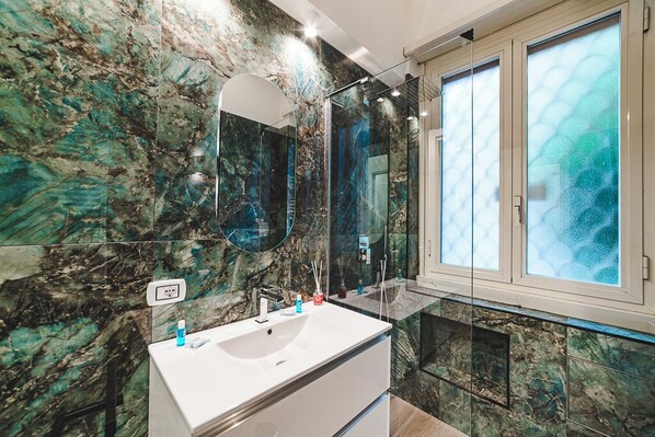A bathroom with a marble wall, a white sink, and a large mirror. - Monteverde Vatican (Rome)