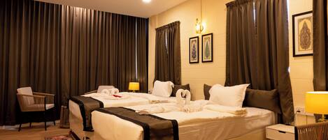 A hotel room with two beds, a desk, a chair, a lamp, and curtains.