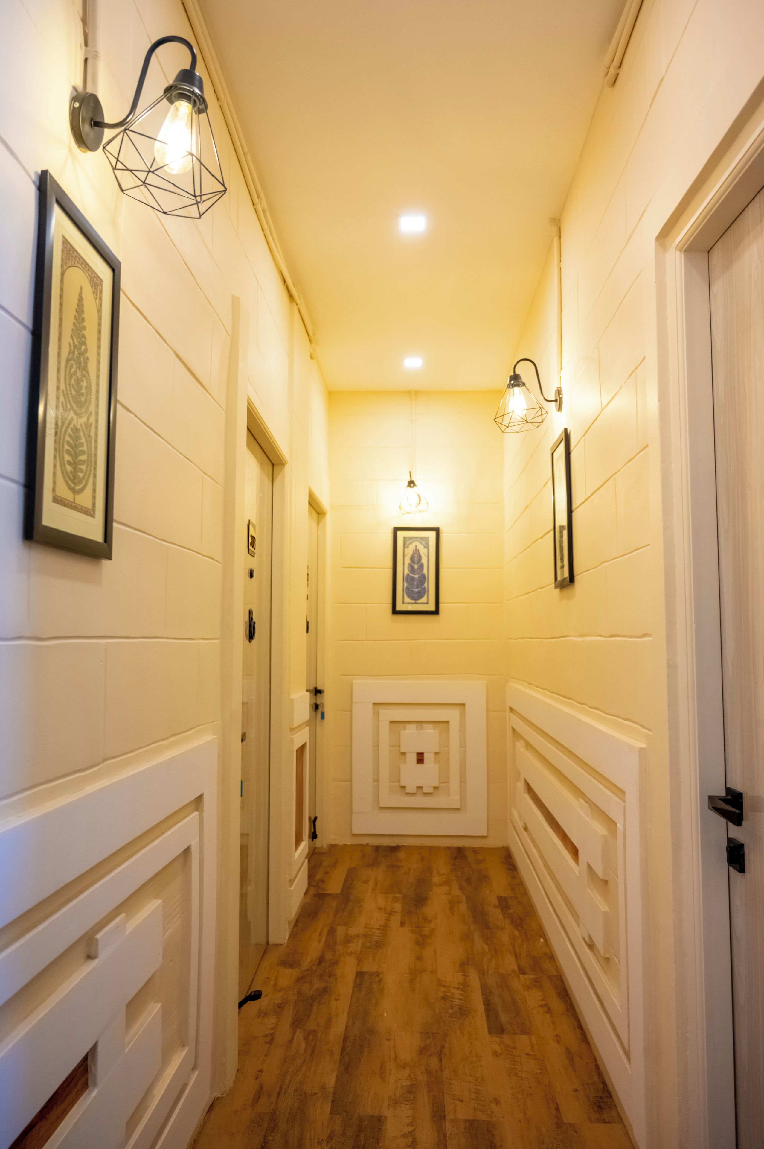 A narrow hallway with wooden flooring, white walls, and framed artwork.