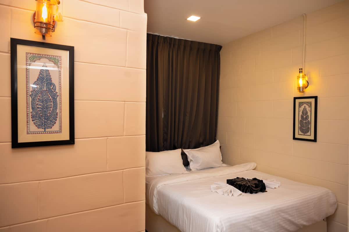 Une chambre d’hôtel avec un lit, une tête de lit, un rideau et deux appliques murales.