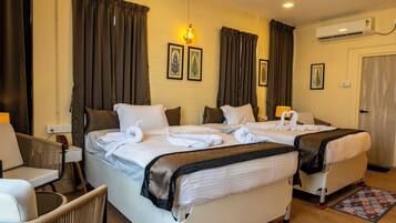 Quarto de hotel com duas camas, uma cadeira, uma mesa e ar condicionado.