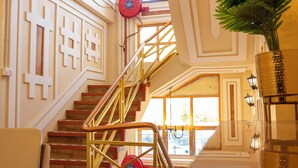 A grand staircase with a red fire extinguisher, a potted plant, and a chair.
