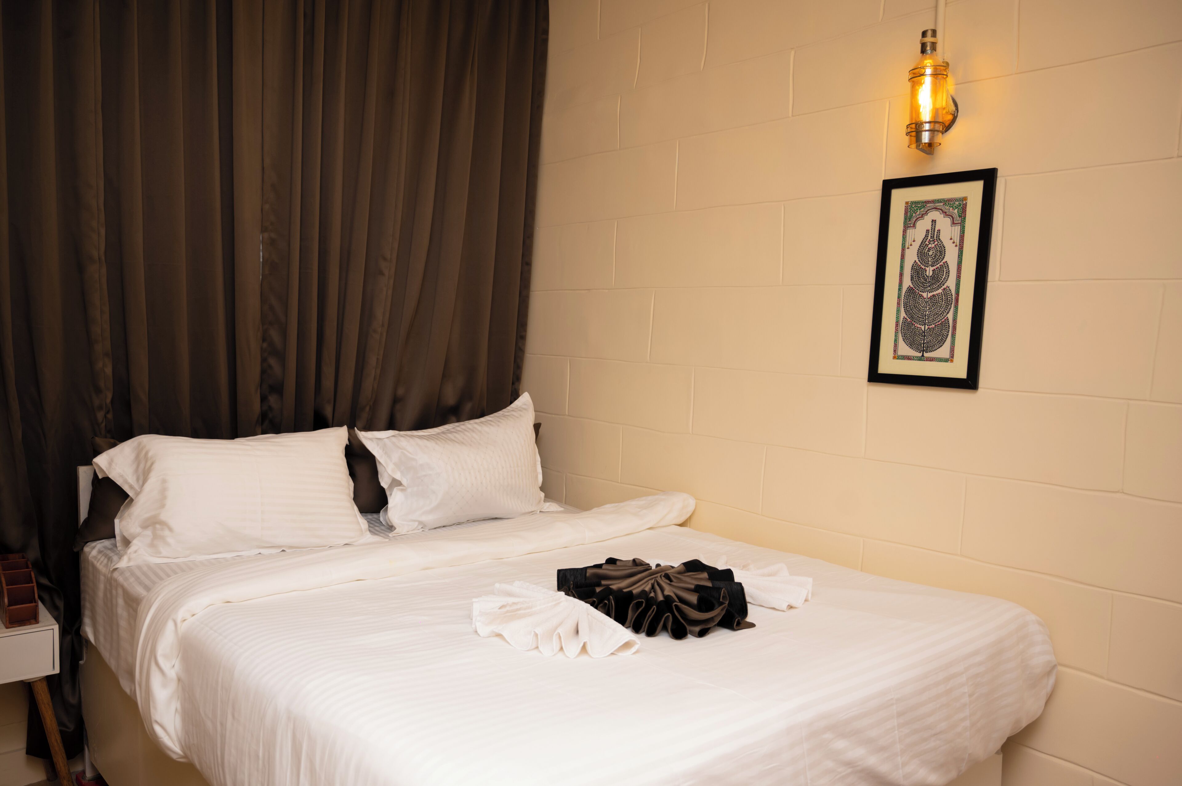 A neatly made bed with white linens, a framed artwork on the wall, and a wall-mounted light fixture.
