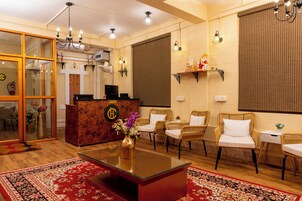 A reception area with a reception desk, wicker chairs, a red carpet, and a chandelier.