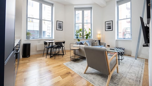 Ein modernes Wohnzimmer mit Sofa, Couchtisch und Sesseln, großen Fenstern und einem Fernseher.