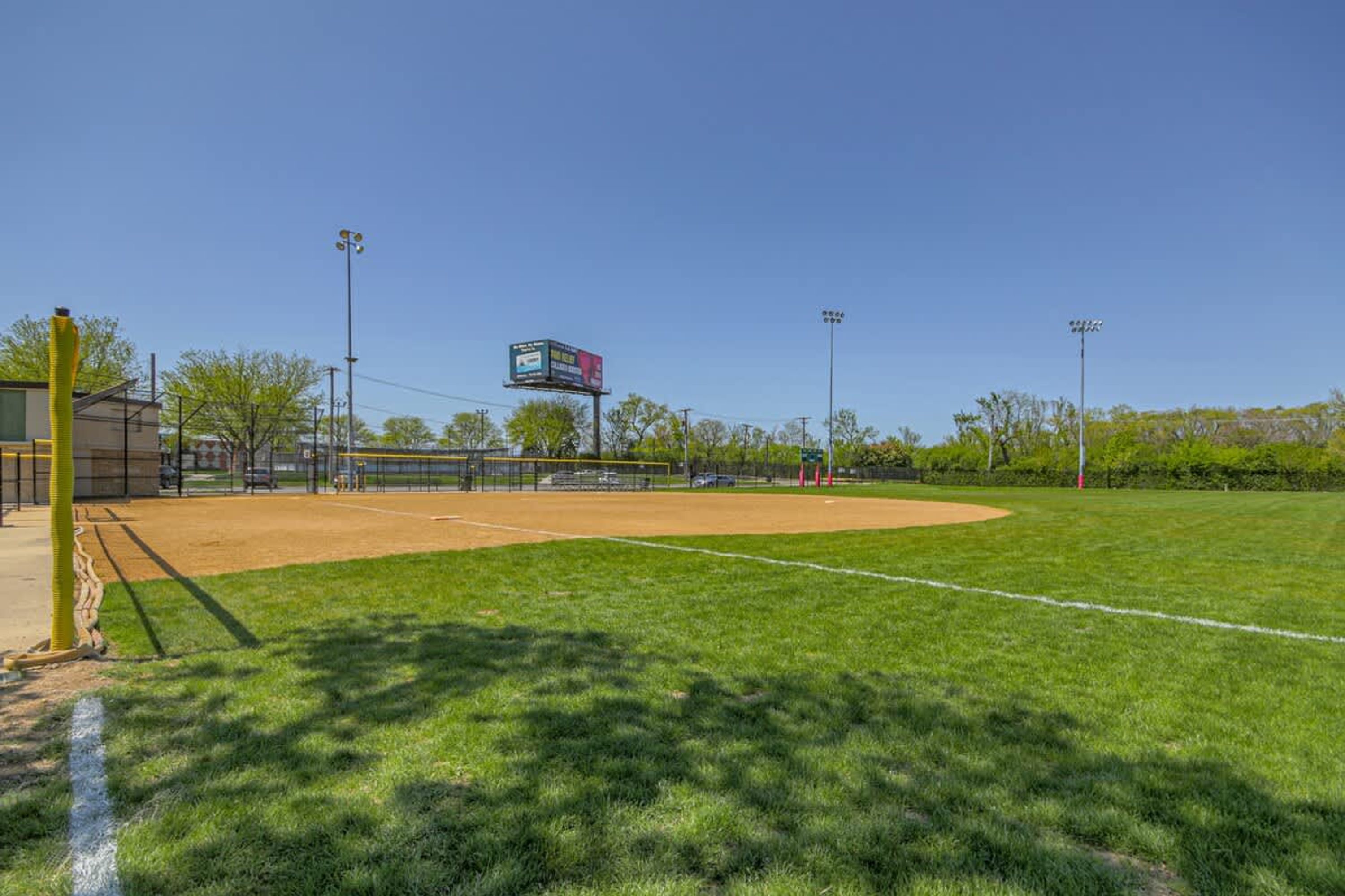 Un campo de béisbol con marcador, focos y cielo despejado.