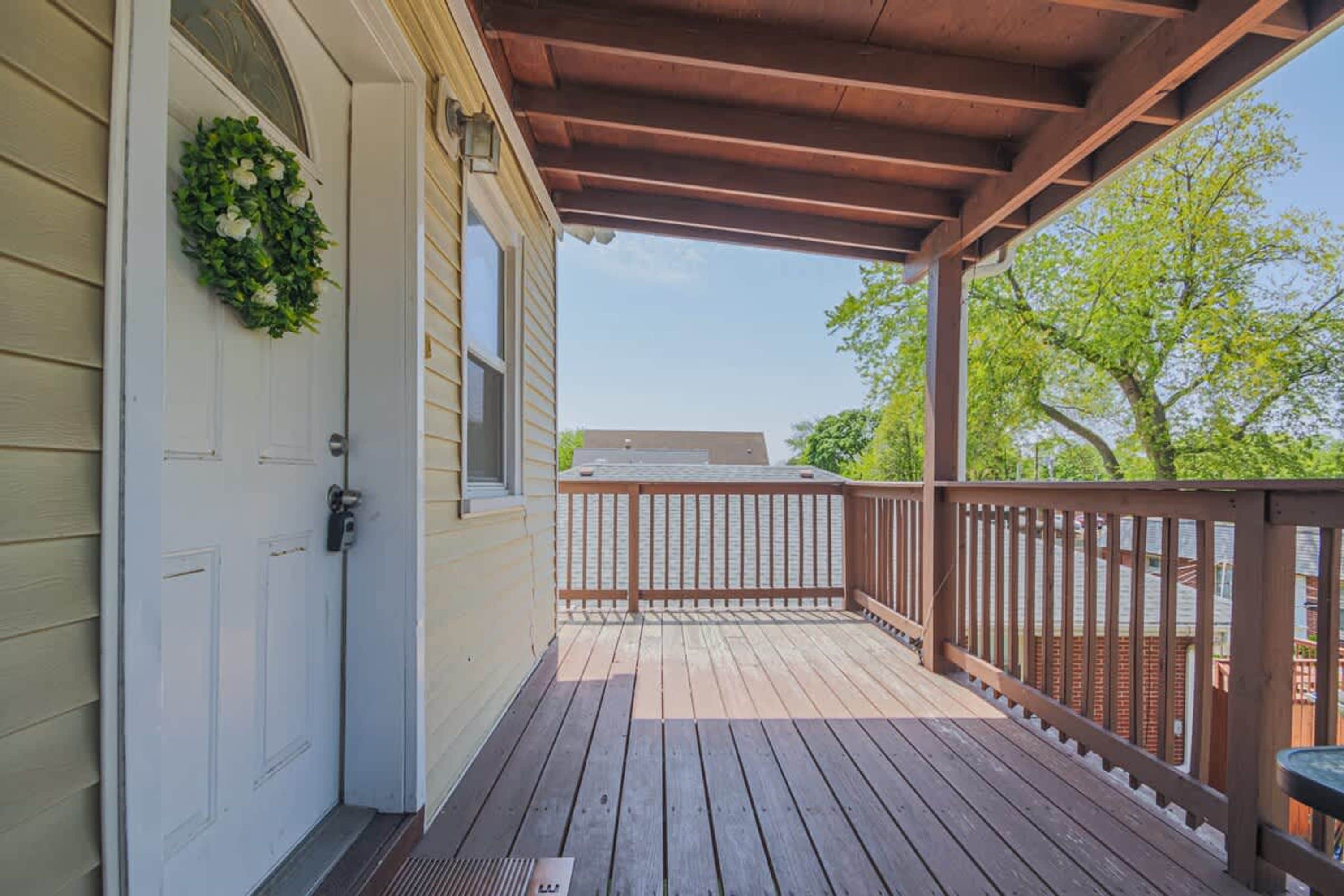 A wooden deck with a railing, a door with a wreath, and a clear sky in the background.