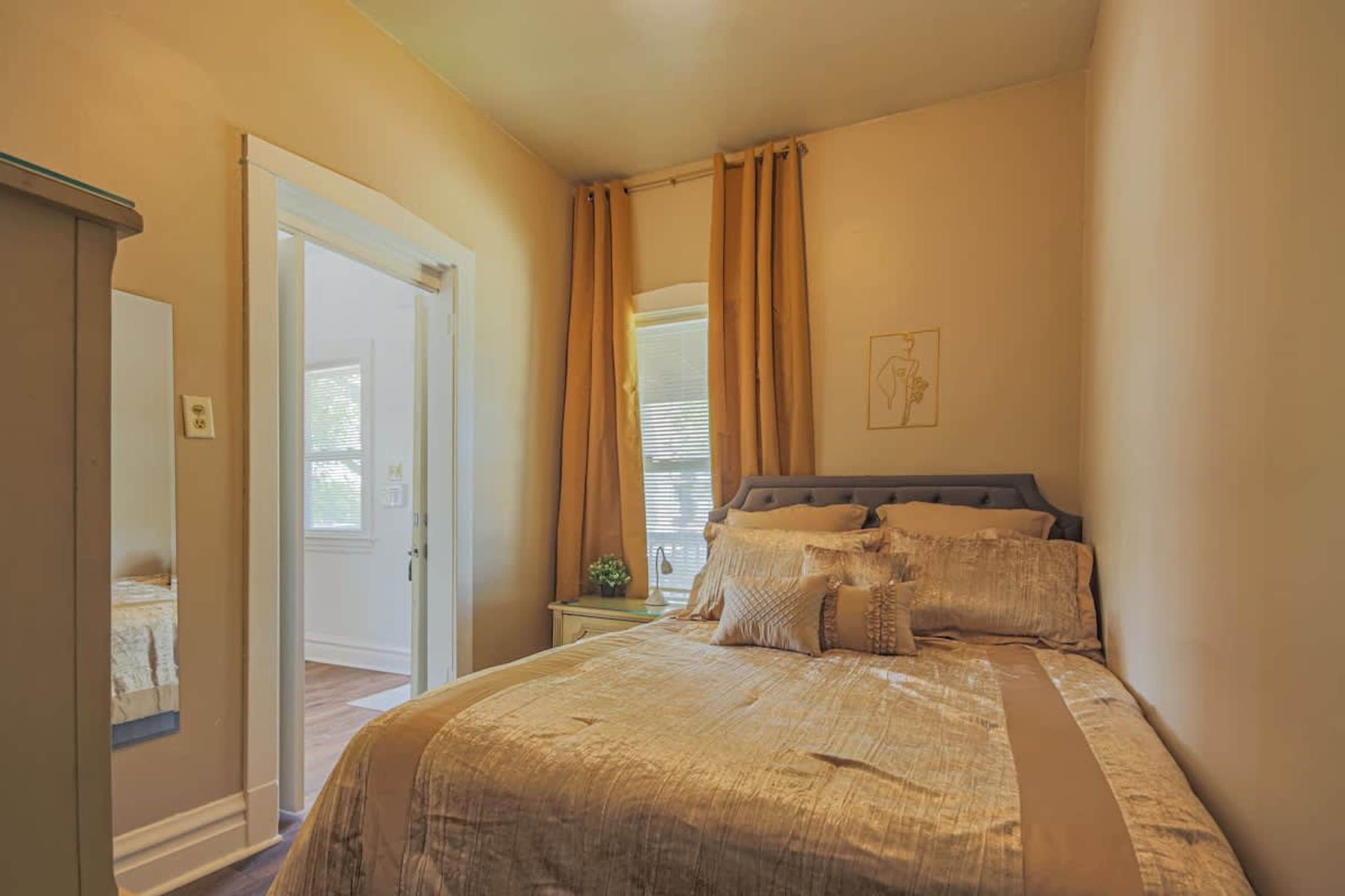 A bedroom with a bed, curtains, a nightstand, and a mirror.