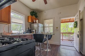 A kitchen with a gas stove, wooden cabinets, a refrigerator, and a dining area with a table and chairs. - Comfy One Bed Apartment in Forest Park (Forest Park)