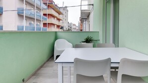 A balcony with a white table and chairs, a potted plant, and a view of neighboring buildings. - Two-room Apartment Scola 12 (Gabicce Mare)