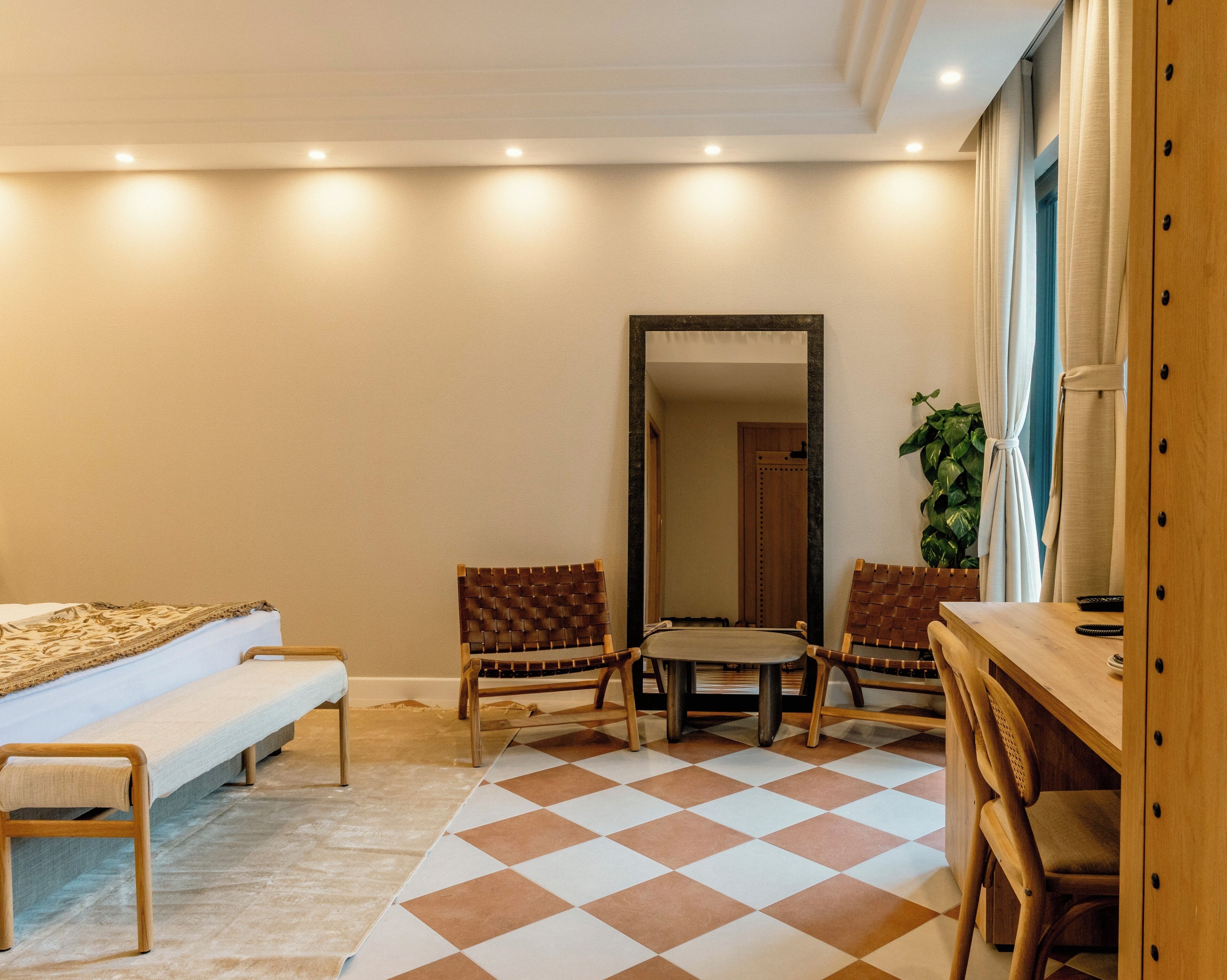 Habitación de hotel con cama, dos sillones, una mesita, espejo y planta en maceta.