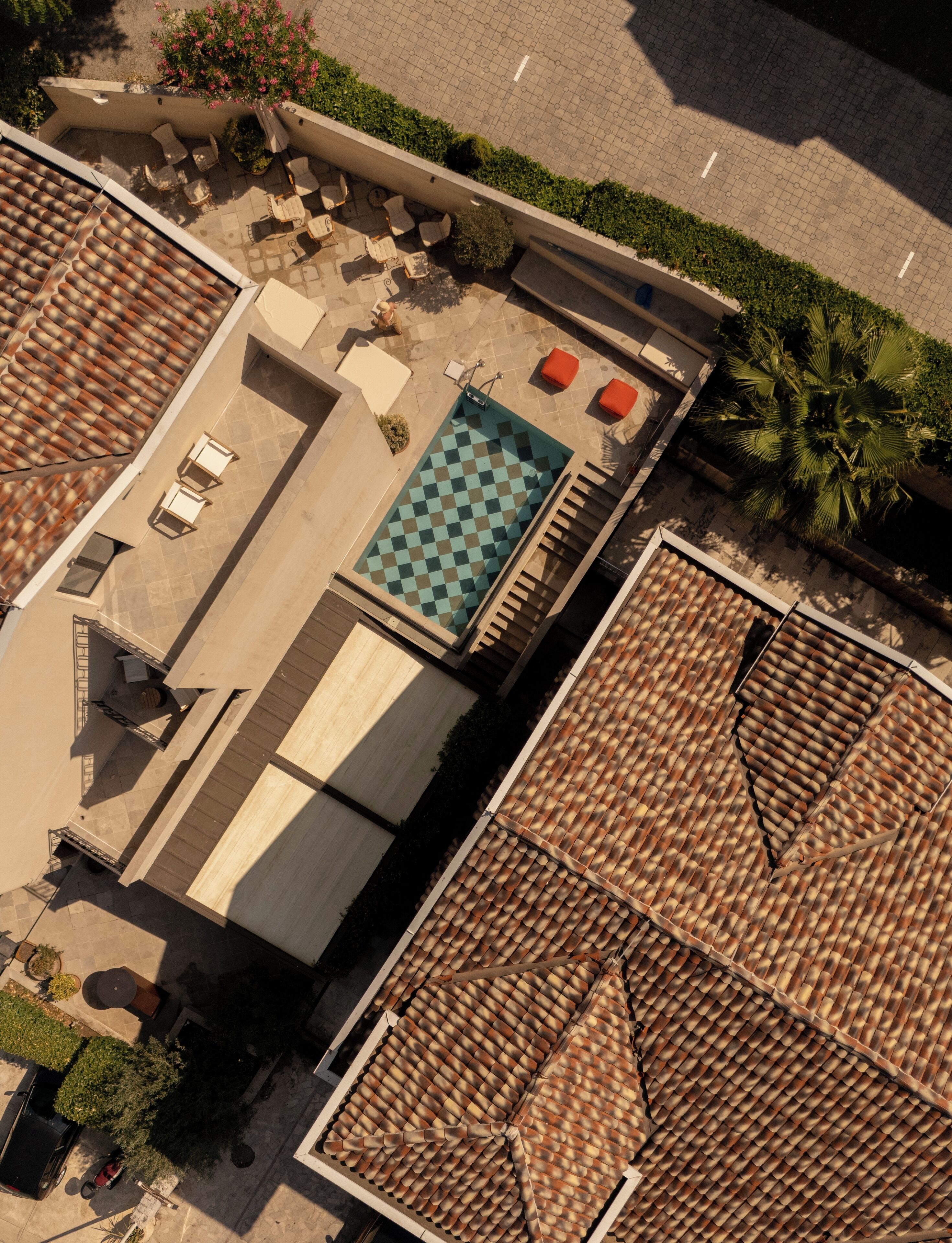An aerial view of a rooftop with a checkered pool, outdoor seating, and a tiled roof.