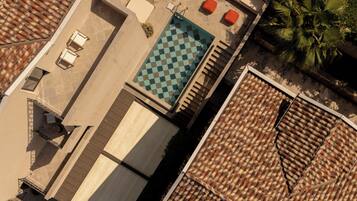 An aerial view of a rooftop with a checkered pool, outdoor seating, and a tiled roof.