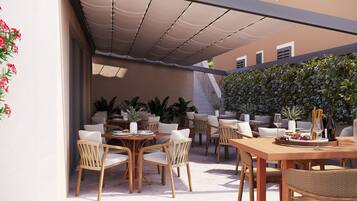 An outdoor patio with wooden tables and chairs, potted plants, and a pergola providing shade.