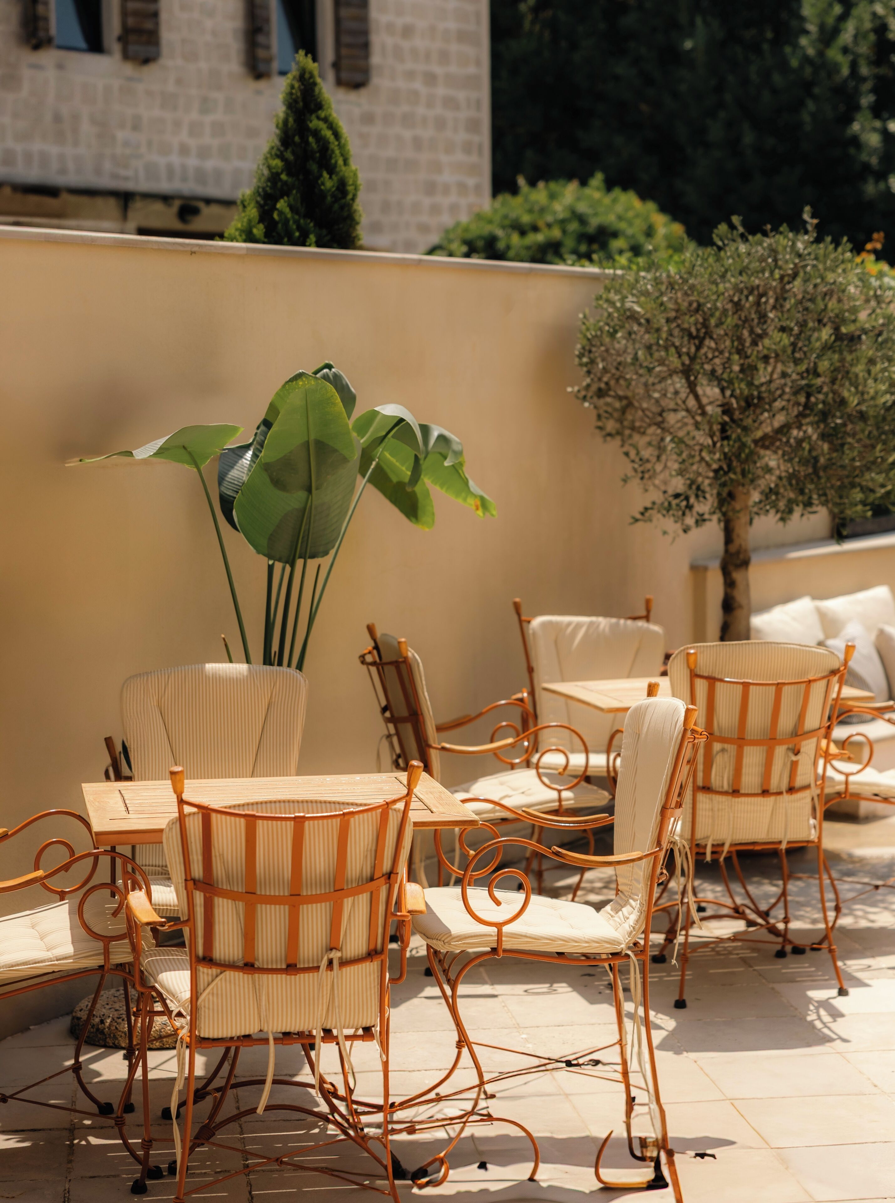 A patio with wicker chairs and a table, surrounded by a low wall and greenery.