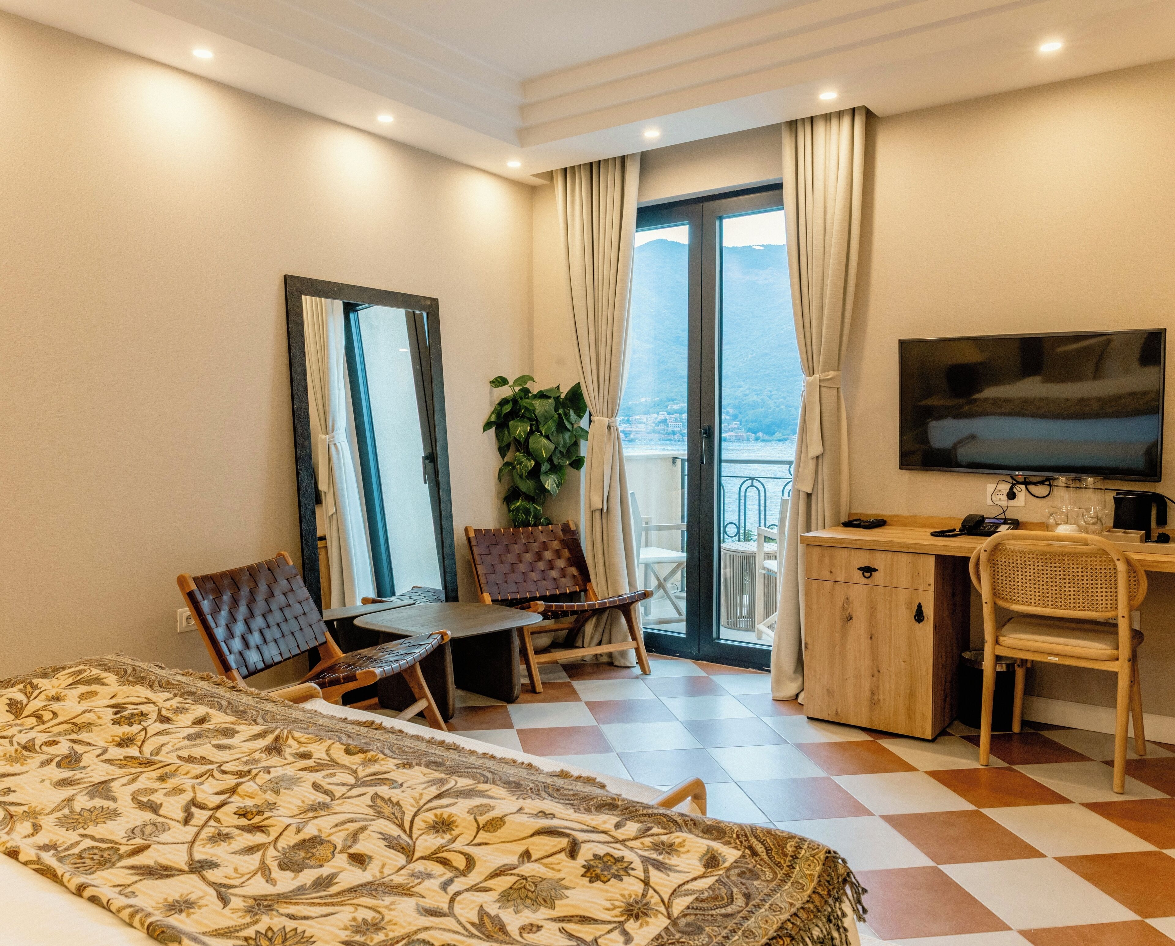 Una habitación de hotel con cama, escritorio, silla, televisor y balcón con vistas.