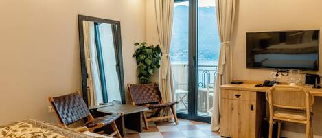 Una habitación de hotel con cama, escritorio, silla, televisor y balcón con vistas.