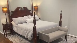 A four-poster bed with a matching bench, a nightstand with a lamp, and a patterned rug. - Stylish In-law Suite in Frederick (Frederick)