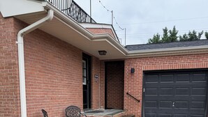 A brick house with a garage, a covered patio with two chairs and a table, and a small front yard. - Stylish In-law Suite in Frederick (Frederick)