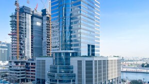 A modern high-rise building with a curved glass facade, surrounded by construction cranes and other buildings. - Luxury 2BR in Merano Tower Stunning City Views (Dubai)