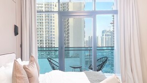 A hotel room with a large bed, a view of the city, and a balcony with chairs. - Luxury 2BR in Merano Tower Stunning City Views (Dubai)