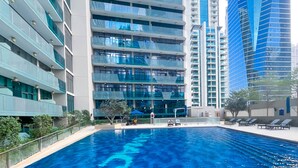 A modern hotel with a swimming pool, multiple balconies, and high-rise buildings in the background. - Luxury 2BR in Merano Tower Stunning City Views (Dubai)