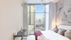 A modern hotel room with a large window, a bed, a bedside table, and a lamp. - Luxury 2BR in Merano Tower Stunning City Views (Dubai)