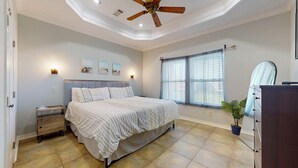 A bedroom with a bed, bedside tables, a ceiling fan, a window with blinds, and a mirror.