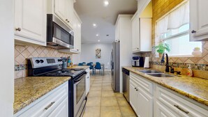 A kitchen with white cabinets, a stove, a microwave, a refrigerator, and a dining area with chairs.