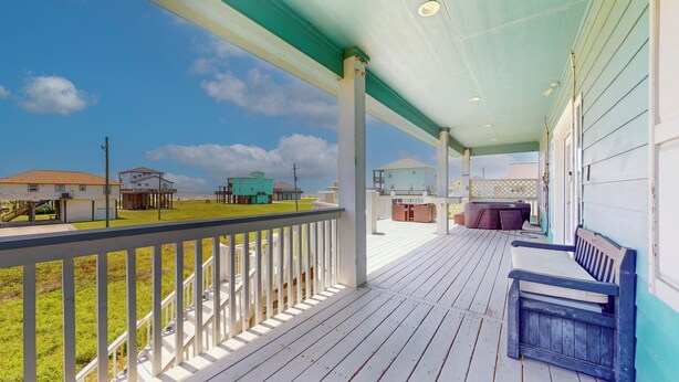 A covered porch with a view of houses and a grassy area.