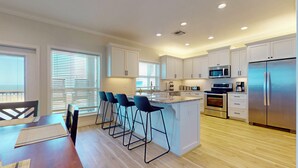 A modern kitchen with white cabinets, stainless steel appliances, and a central island with bar stools. - At Tides Edge: 3  BR, 3  BA House in Crystal Beach, Sleeps 12 (Bolivar Peninsula)