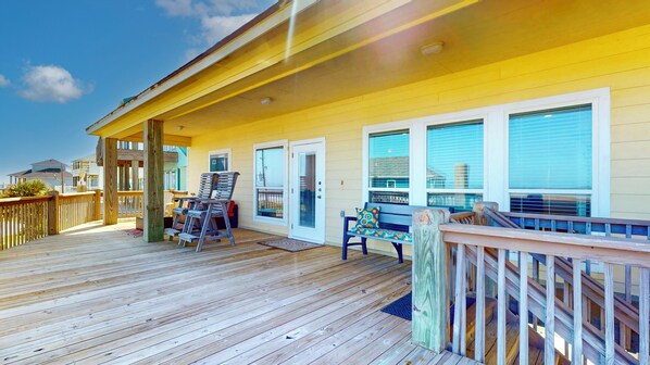 A wooden deck with a covered area, a bench, and a chair.