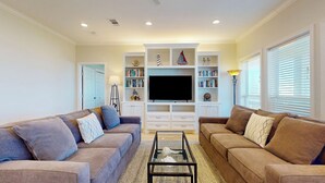 A living room with two sofas, a coffee table, a TV, and built-in bookshelves. - At Tides Edge: 3  BR, 3  BA House in Crystal Beach, Sleeps 12 (Bolivar Peninsula)