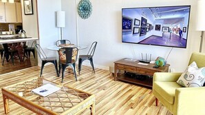 Ein modernes Wohnzimmer mit Essbereich, einem an der Wand befestigten Flachbildfernseher und einem Holztisch.
