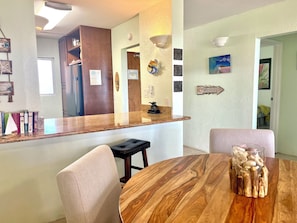 A modern kitchen with a wooden countertop, a dining table with chairs, and a decorative centerpiece. - Hotel-zoned Maui True Paradise - Menehune Shores 227 (Kihei)