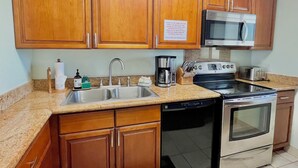 A kitchen with wooden cabinets, a stainless steel sink, a coffee maker, a toaster, and an oven.