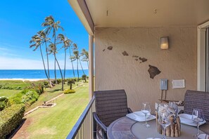 A balcony with a table set for dining, overlooking a beach with palm trees and the ocean.
