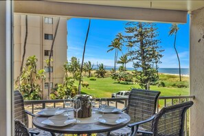 A balcony with a table set for two, overlooking a golf course and ocean view.