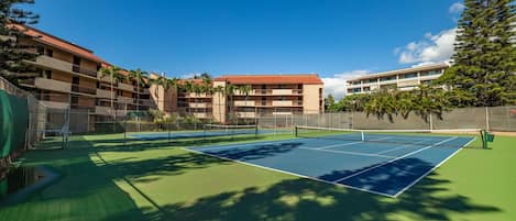 A tennis court with a net, surrounded by a fence, and adjacent to a building with multiple balconies.
