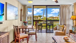 Habitación de hotel con balcón, comedor y zona de estar con vistas al océano y edificios.