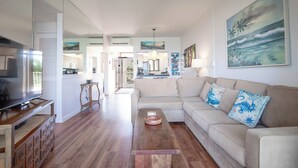 Amplia sala de estar con televisor de pantalla plana, una mesa de centro de madera y un sofá color beige con almohadones decorativos.