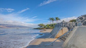 Una playa con una escalera de hormigón que baja hasta la orilla, palmeras y un cielo despejado.