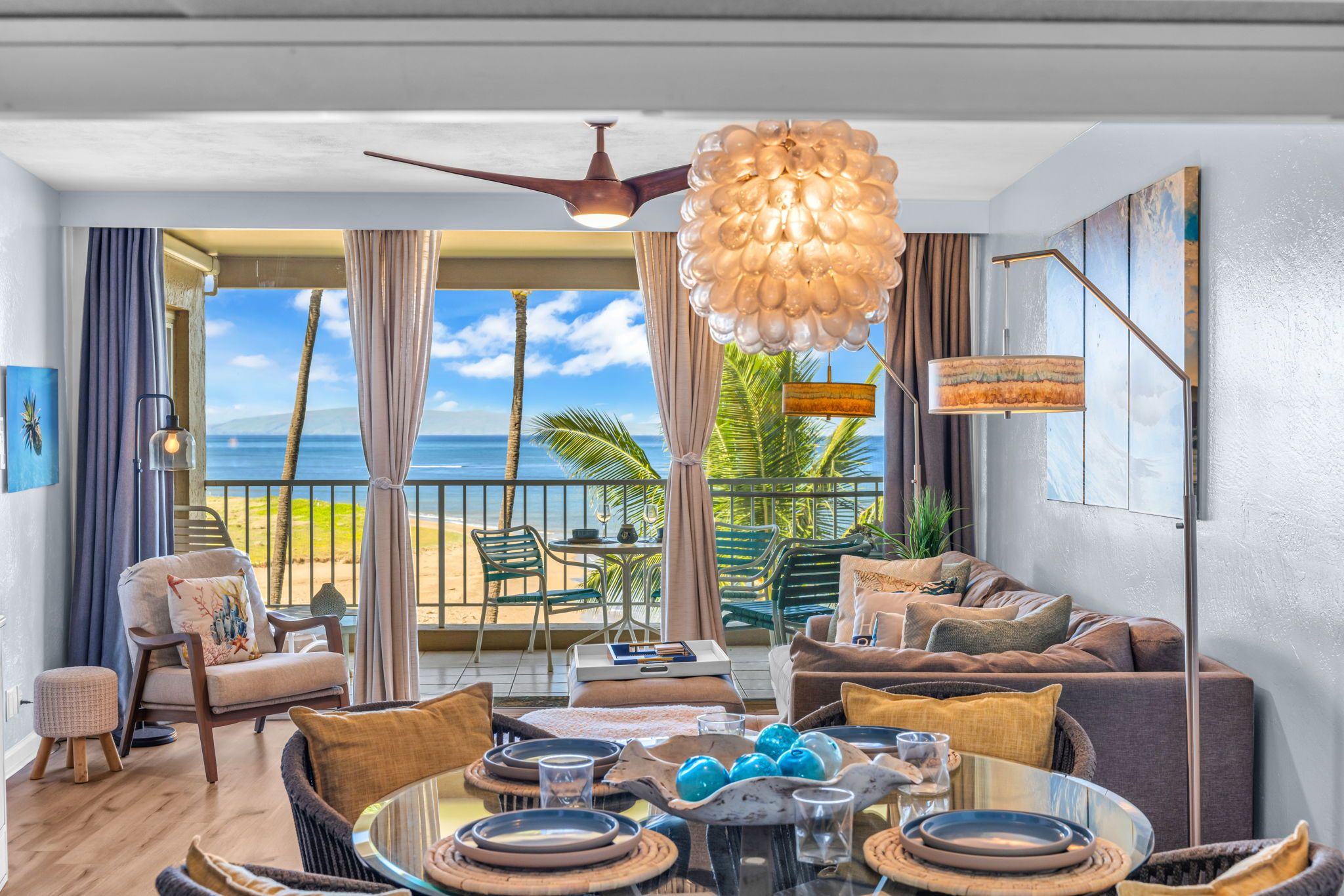 A spacious living area with a view of the ocean, a balcony with outdoor seating, and a ceiling fan.