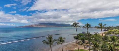 Un resort en la playa con vista despejada al océano, palmeras y una montaña distante.
