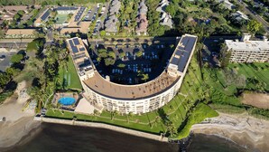 An aerial view of a resort with a curved building, a swimming pool, and a beach. - FALL SPECIAL!! PREMIUM OCEANFRONT UNIT WHER THE OCEAN MEETS THE SKY!!! (Kihei)