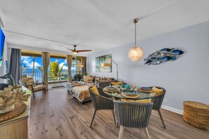 A spacious living area with a balcony, a dining table set for four, and a ceiling fan. - Stunning Premium Direct Ocean Front Escape! (Kihei)