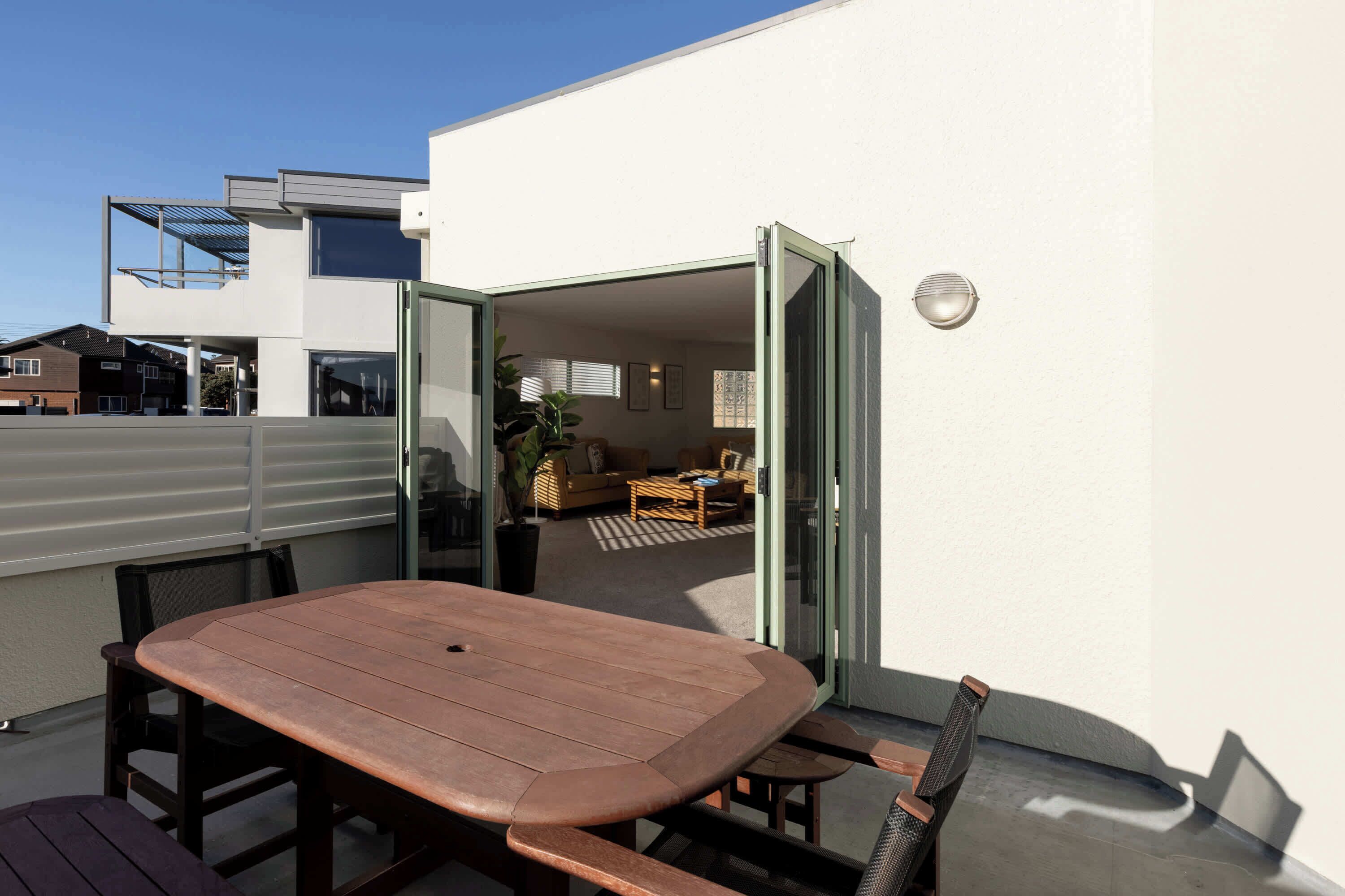 An outdoor patio with a wooden table and benches, a sliding glass door leading to an interior living area with a sofa and coffee table.