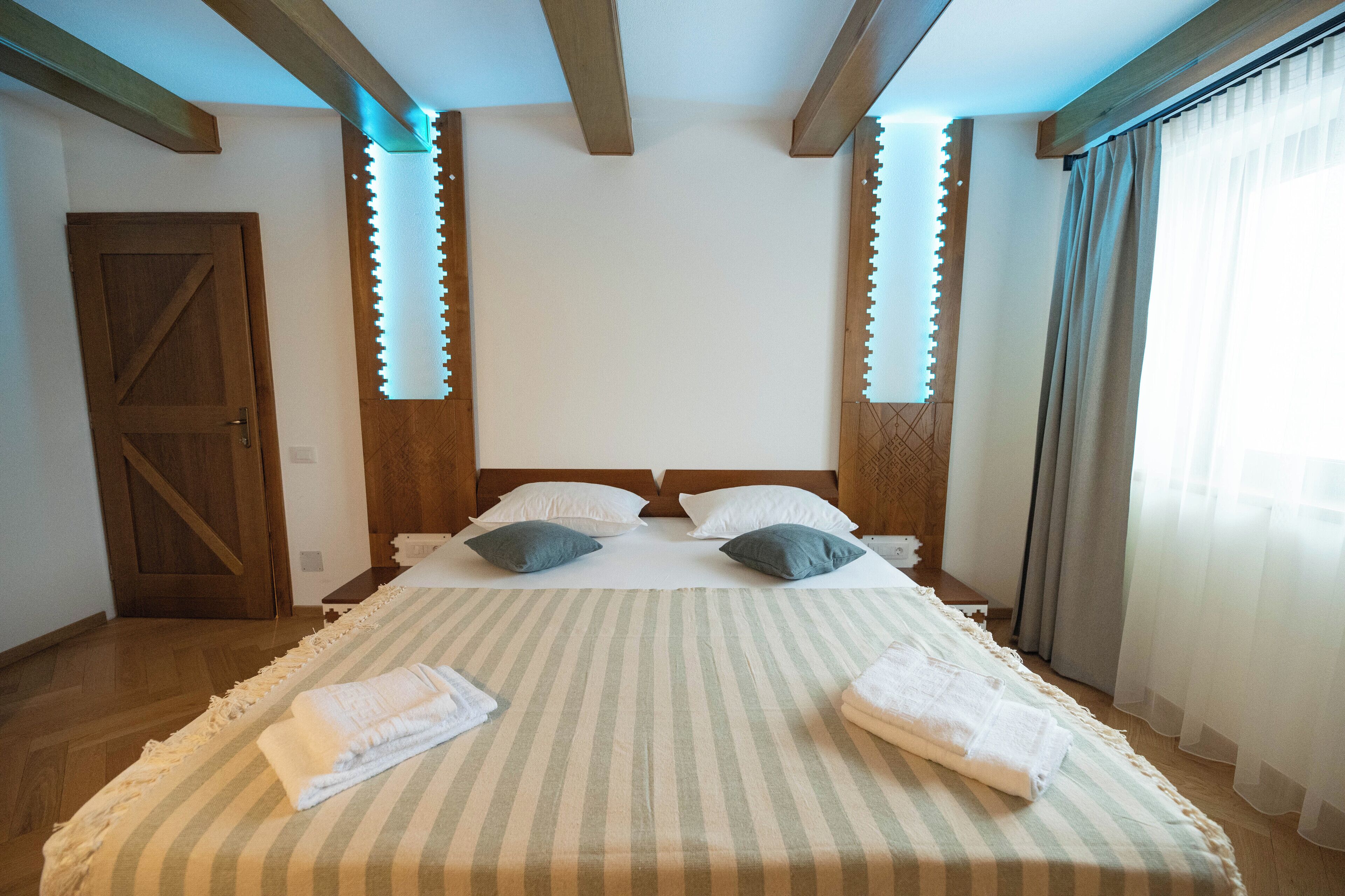 Une chambre d’hôtel avec un grand lit, des poutres en bois au plafond, une porte en bois et des rideaux aux fenêtres.