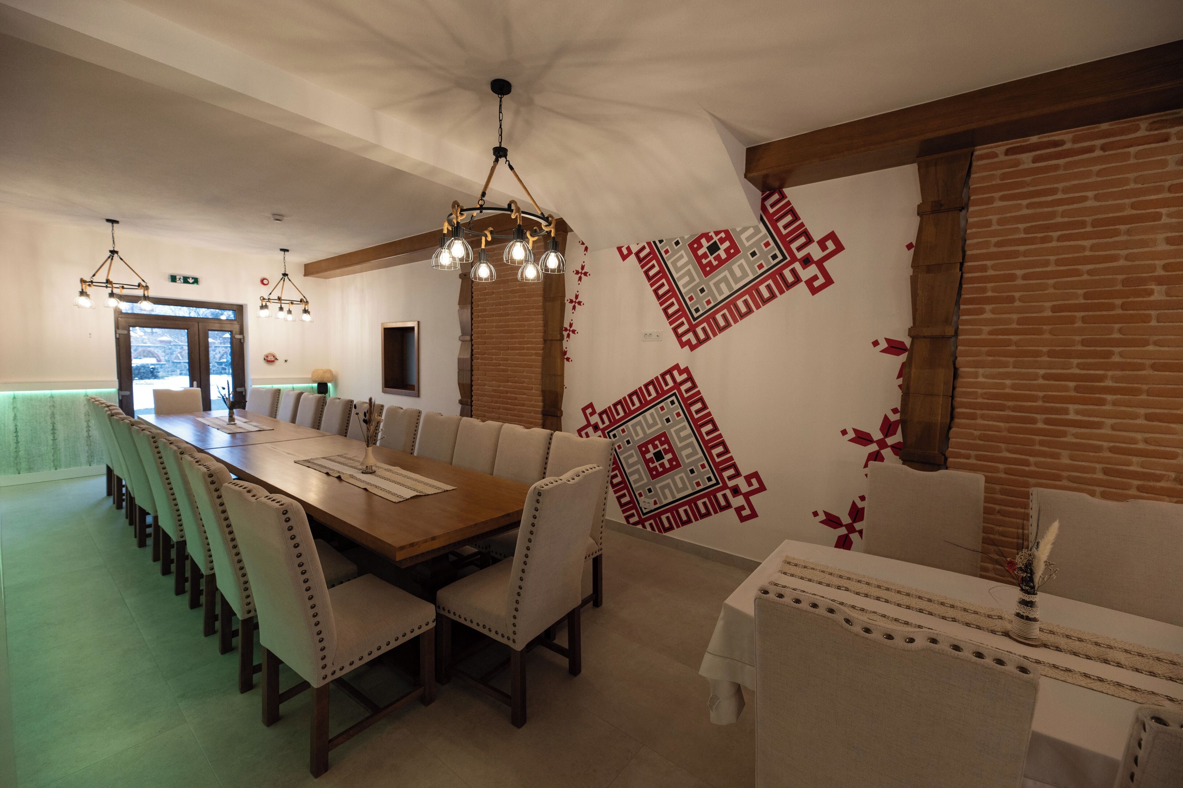 Un comedor con una larga mesa de madera, sillas con cojines y un muro con diseño.